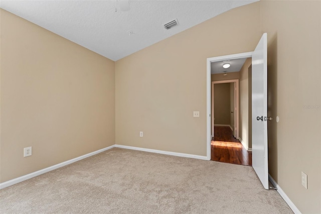 empty room with lofted ceiling, light colored carpet, and a textured ceiling