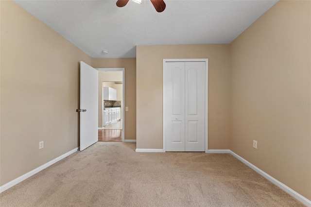 unfurnished bedroom with ceiling fan, light colored carpet, a textured ceiling, and a closet