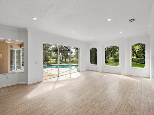 interior space with ornamental molding, a wealth of natural light, a textured ceiling, and light hardwood / wood-style floors