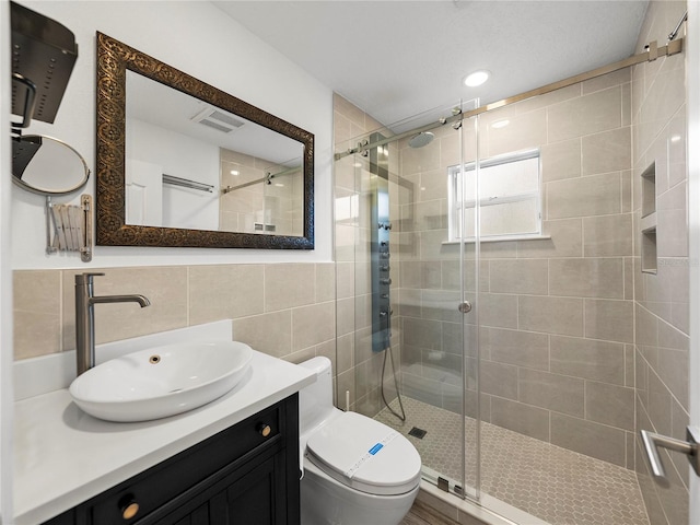 bathroom with toilet, tile walls, vanity, a shower with door, and backsplash