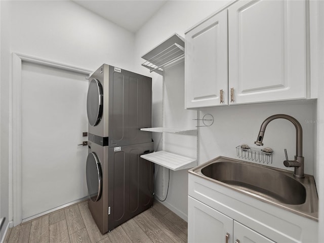 laundry area with stacked washer / dryer, sink, cabinets, and light hardwood / wood-style floors