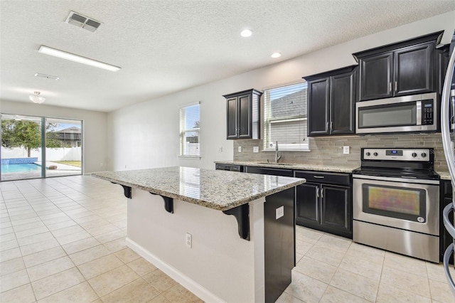 kitchen featuring sink, a kitchen island, stainless steel appliances, light stone countertops, and a kitchen bar