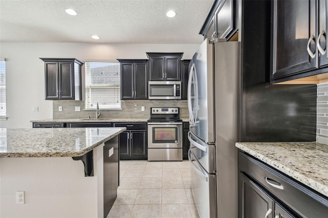 kitchen with sink, light tile patterned floors, appliances with stainless steel finishes, a kitchen breakfast bar, and light stone countertops