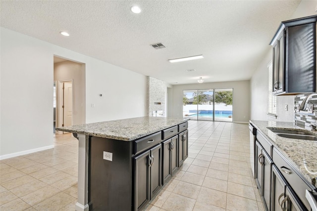 kitchen with light stone countertops, a kitchen island, sink, and light tile patterned floors