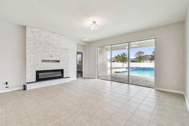 unfurnished living room with light tile patterned flooring, a stone fireplace, and a textured ceiling