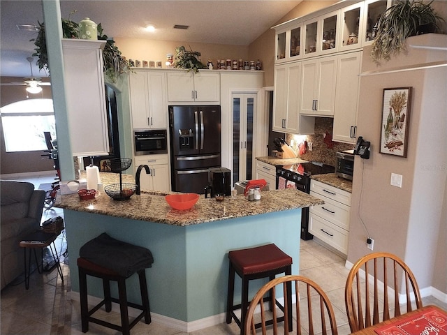 kitchen featuring white cabinetry, dark stone countertops, a kitchen breakfast bar, and black appliances