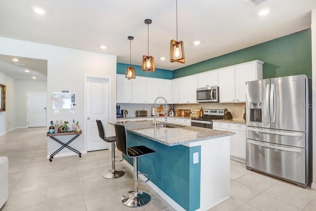 kitchen with sink, white cabinetry, stainless steel appliances, light stone countertops, and a kitchen island with sink