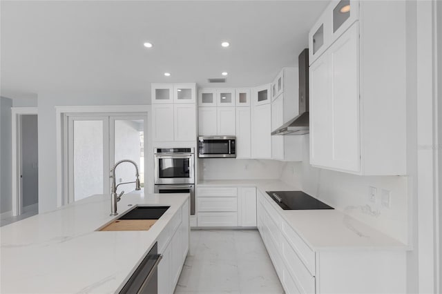 kitchen with wall chimney exhaust hood, sink, light stone counters, appliances with stainless steel finishes, and white cabinets