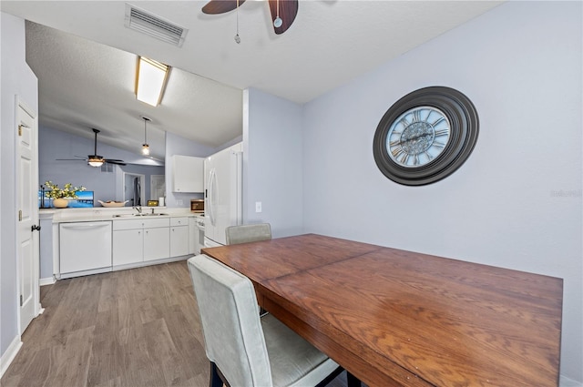 dining area with a textured ceiling, light hardwood / wood-style flooring, ceiling fan, and vaulted ceiling