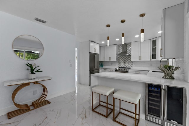 kitchen featuring high quality appliances, tasteful backsplash, wine cooler, kitchen peninsula, and wall chimney exhaust hood