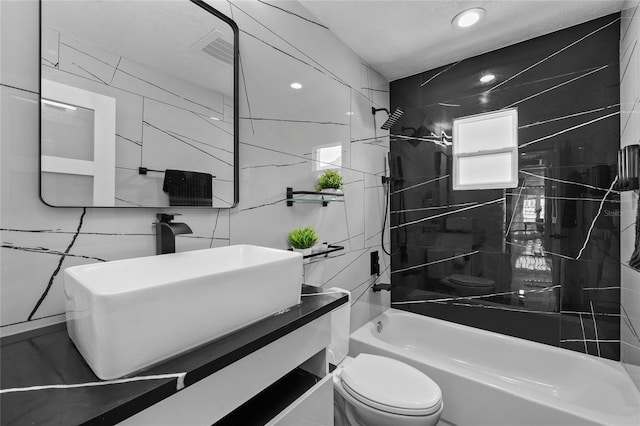 full bathroom featuring tiled shower / bath, tile walls, vanity, toilet, and a textured ceiling