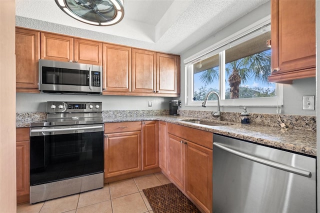 kitchen with light tile patterned flooring, appliances with stainless steel finishes, sink, light stone counters, and a textured ceiling