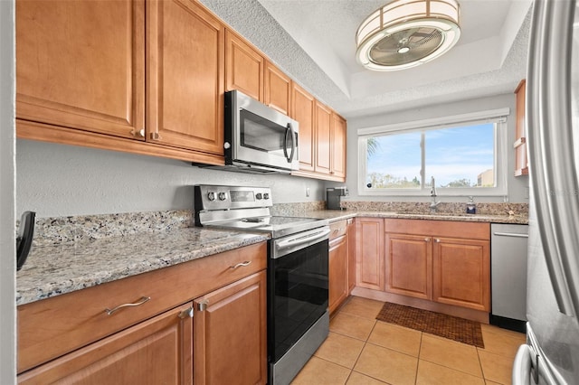 kitchen with sink, a textured ceiling, light tile patterned floors, a raised ceiling, and stainless steel appliances