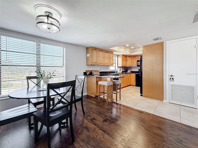 dining space featuring a raised ceiling, a textured ceiling, and light hardwood / wood-style floors