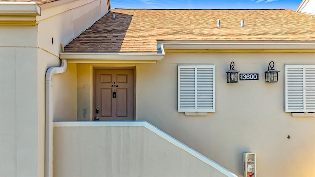 property entrance with a shingled roof and stucco siding