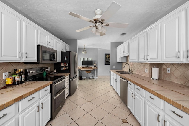 kitchen with stainless steel appliances, white cabinetry, sink, and tile countertops