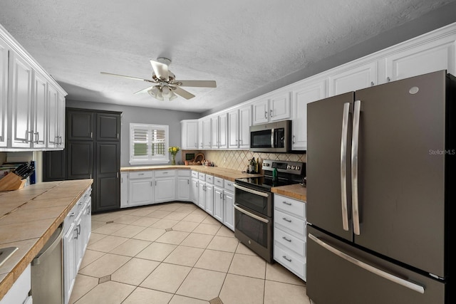 kitchen featuring stainless steel appliances, tasteful backsplash, tile counters, white cabinets, and light tile patterned flooring