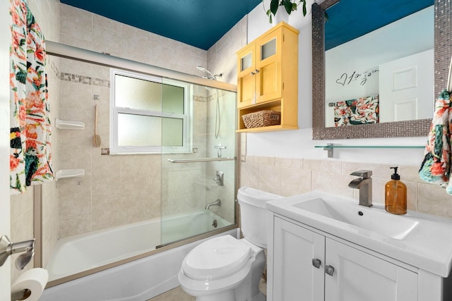 full bath with toilet, shower / bath combination with glass door, vanity, and tile walls