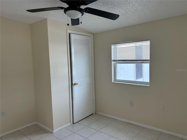 unfurnished bedroom with ceiling fan, a closet, light tile patterned flooring, and a textured ceiling