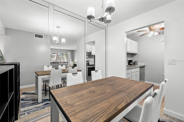 dining room with sink, light wood-type flooring, ceiling fan with notable chandelier, and a textured ceiling