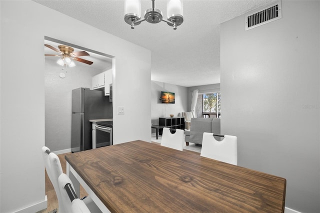 dining space with ceiling fan with notable chandelier and a textured ceiling