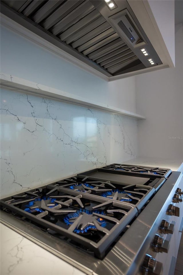 interior details with backsplash, wall chimney range hood, and cooktop