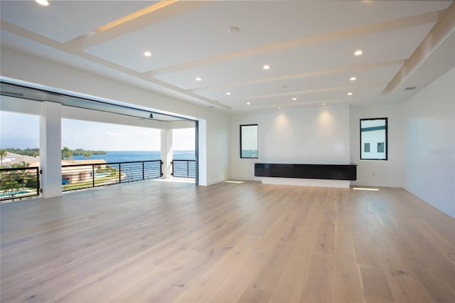 unfurnished living room with a raised ceiling, a water view, and light hardwood / wood-style floors