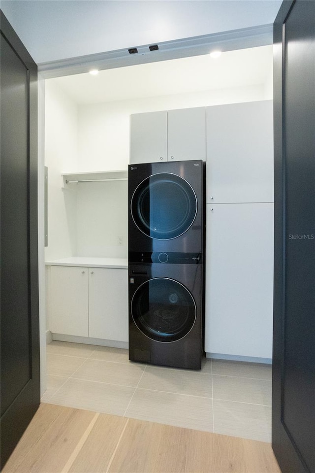 laundry room featuring cabinets, stacked washing maching and dryer, and light hardwood / wood-style flooring