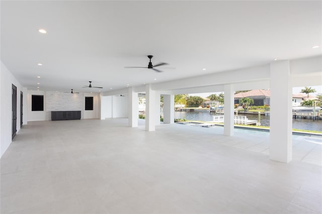 unfurnished living room featuring a water view, ceiling fan, and a fireplace