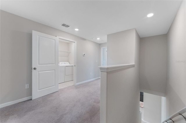 hall with separate washer and dryer and light colored carpet