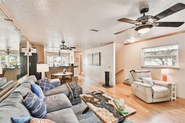 living room with ceiling fan, ornamental molding, light hardwood / wood-style floors, and a textured ceiling