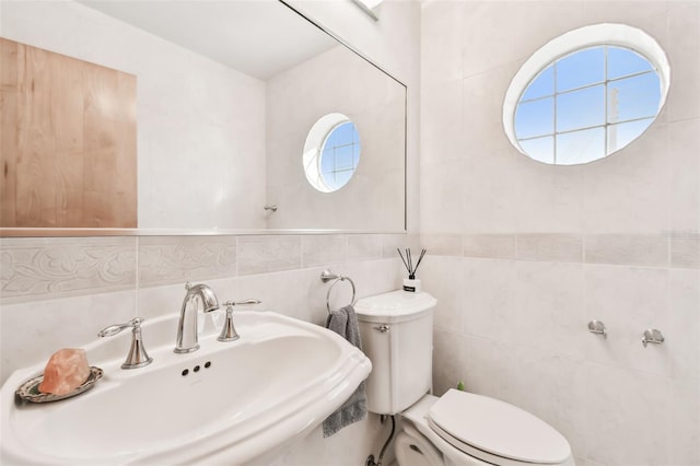 bathroom with decorative backsplash, toilet, sink, and tile walls