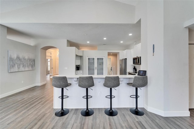 kitchen featuring appliances with stainless steel finishes, white cabinetry, wood-type flooring, a kitchen breakfast bar, and kitchen peninsula