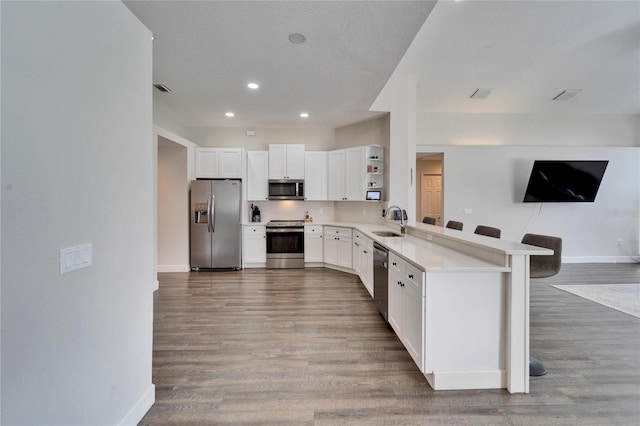 kitchen featuring sink, white cabinetry, hardwood / wood-style floors, stainless steel appliances, and kitchen peninsula