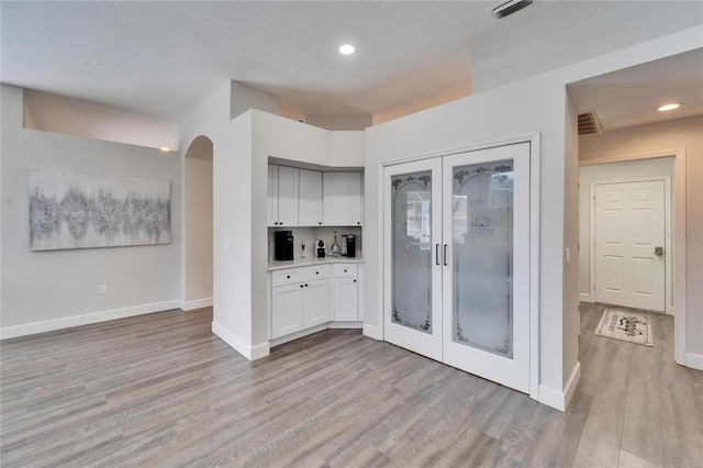 kitchen featuring white cabinetry, a textured ceiling, light hardwood / wood-style floors, and french doors