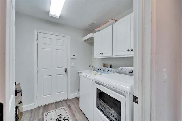 laundry room featuring light hardwood / wood-style floors, washing machine and dryer, cabinets, and a textured ceiling