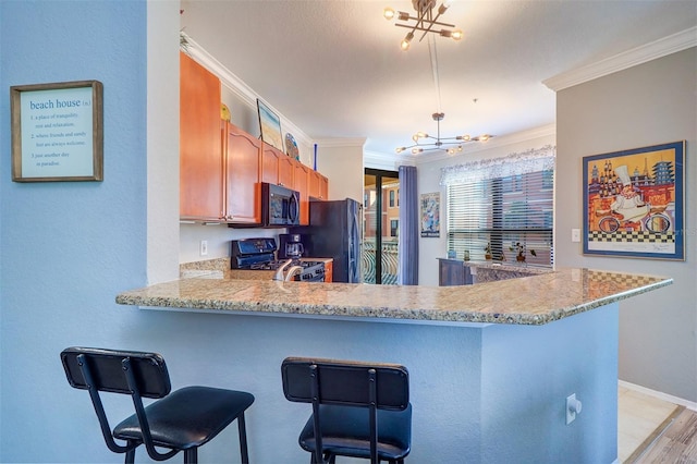 kitchen with crown molding, an inviting chandelier, gas range oven, black fridge, and kitchen peninsula