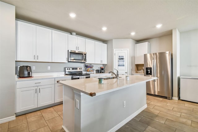 kitchen featuring white cabinetry, sink, light stone counters, stainless steel appliances, and a center island with sink