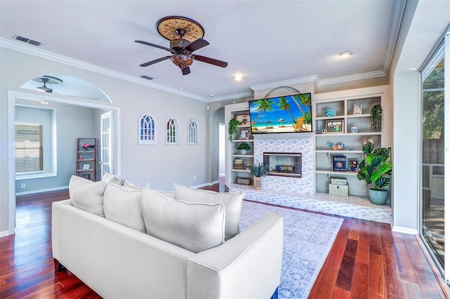 living room featuring dark hardwood / wood-style floors, a fireplace, ornamental molding, ceiling fan, and built in shelves