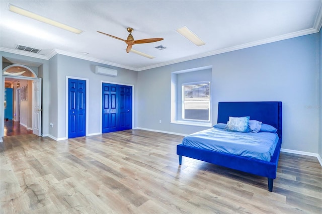 bedroom with ceiling fan, a wall mounted AC, ornamental molding, light hardwood / wood-style floors, and two closets