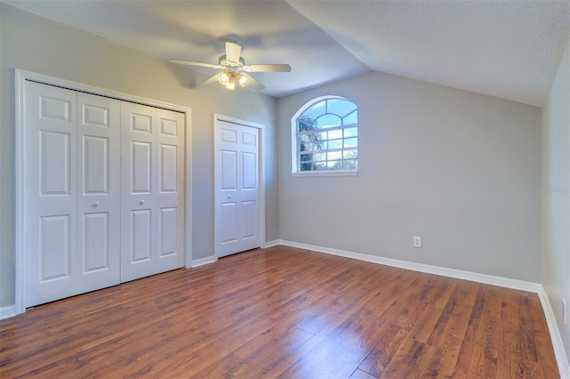 unfurnished bedroom featuring multiple closets, lofted ceiling, dark hardwood / wood-style floors, and ceiling fan