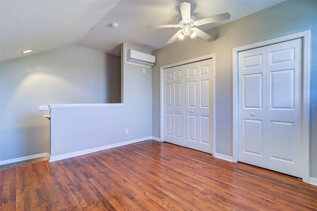 unfurnished bedroom featuring a wall mounted air conditioner, vaulted ceiling, multiple closets, dark hardwood / wood-style floors, and ceiling fan