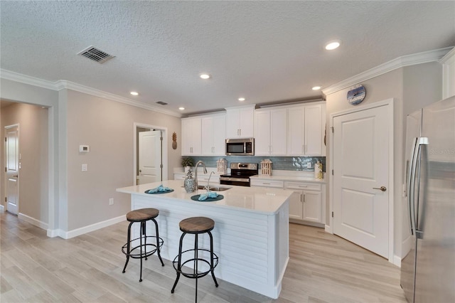 kitchen with white cabinets, stainless steel appliances, backsplash, and a kitchen island with sink