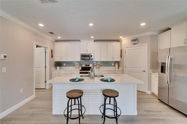 kitchen with white cabinetry, appliances with stainless steel finishes, a kitchen island with sink, and a kitchen breakfast bar