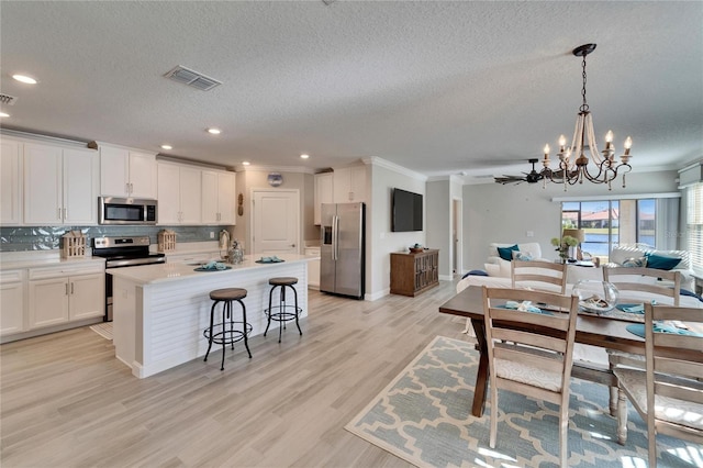 kitchen with appliances with stainless steel finishes, light hardwood / wood-style flooring, tasteful backsplash, a chandelier, and ornamental molding