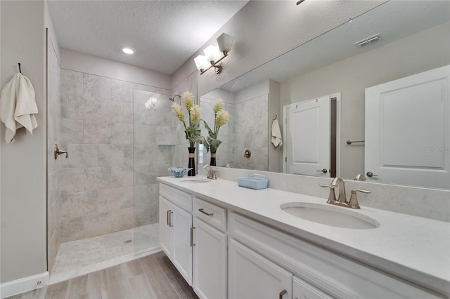 bathroom with wood-type flooring, tiled shower, a textured ceiling, and vanity