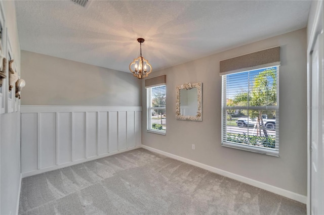 carpeted empty room featuring a textured ceiling and a notable chandelier