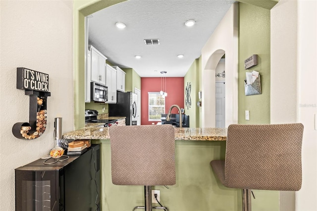 kitchen with stainless steel appliances, a kitchen bar, hanging light fixtures, and white cabinets