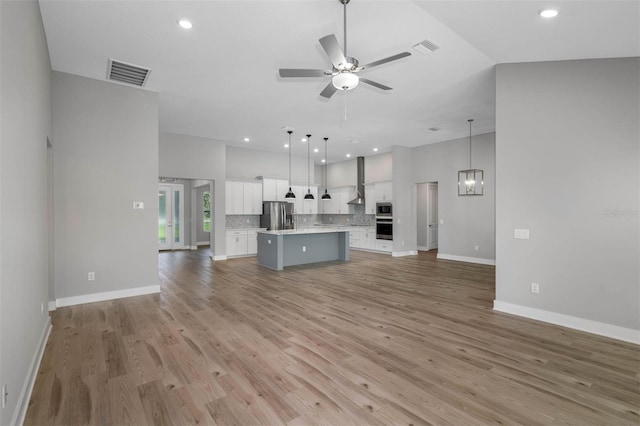 unfurnished living room with ceiling fan with notable chandelier and light hardwood / wood-style flooring