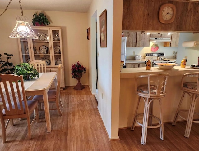 kitchen featuring stove, hanging light fixtures, a breakfast bar area, and light hardwood / wood-style floors